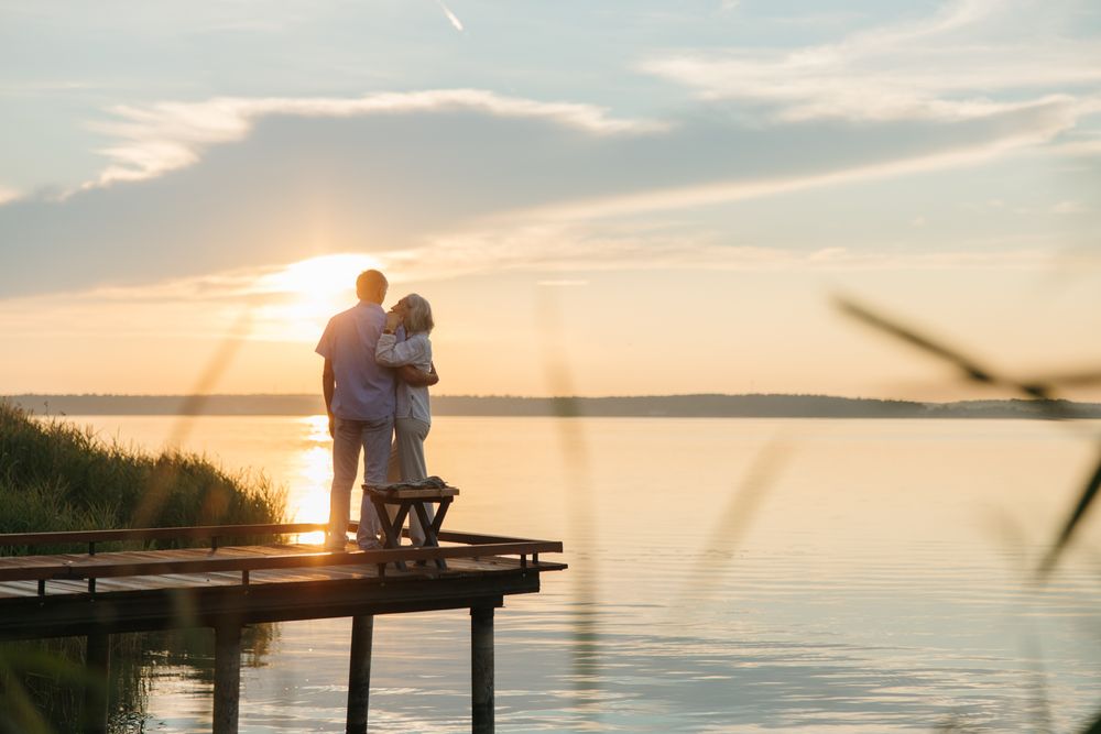 Älteres Paar steht bei Sonnenuntergang auf einem Steg am See
